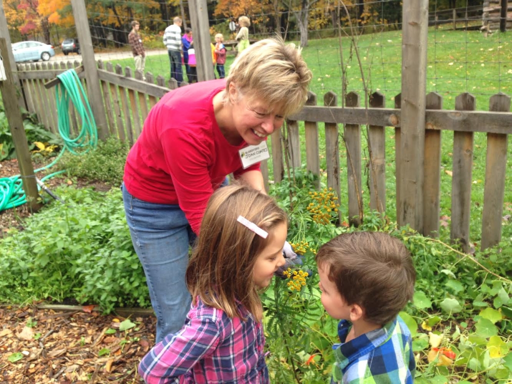 Blandford Nature Center volunteer Joan Coates holds one of the herbs from the Center’s garden for her small visitors to smell.  Last year volunteers like Joan, who was pruning the garden, contributed 12,000 hours to Blandford.